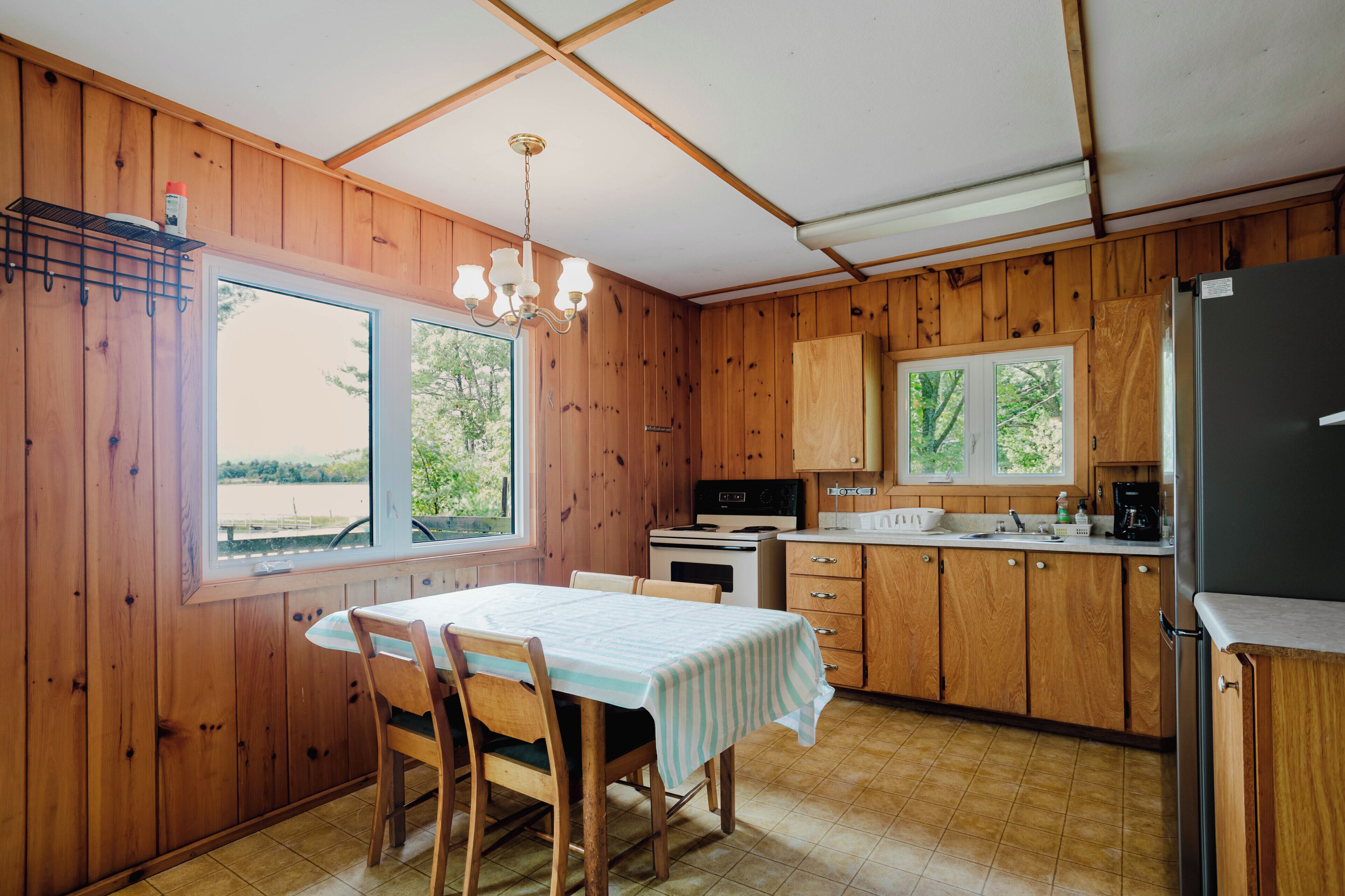 Une cuisine avec des murs en bois, une table à manger avec des chaises, un réfrigérateur et une fenêtre donnant sur un paysage.