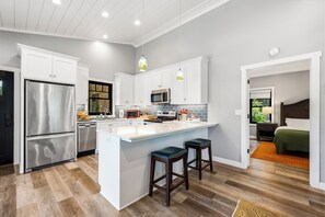 Une cuisine moderne avec des meubles blancs, des appareils en acier inoxydable et un grand îlot central doté de tabourets.