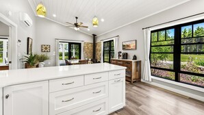 A spacious kitchen with a large island, wooden cabinets, and a view of the outdoors through large windows. - Modern Rustric Retreat w/Fenced Yard + 4-Season Room (Baileys Harbor)