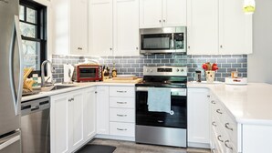 A modern kitchen with white cabinetry, a stainless steel refrigerator, a microwave, a stove, and a dishwasher. - Modern Rustric Retreat w/Fenced Yard + 4-Season Room (Baileys Harbor)