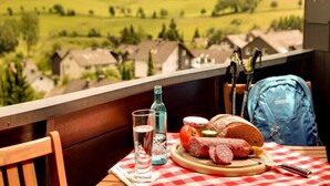A balcony with a table set for a meal, a view of a village, and a blue backpack. - 2 Person Holiday Park Home in Willingen (Willingen)