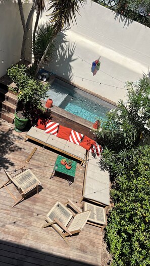 Un espace aménagé au bord de la piscine, avec une terrasse en bois, des chaises longues, une petite table et des plantes en pot.