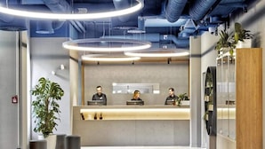 Zona de recepción con diseño moderno, que incluye un mostrador de recepción, tres empleados y una planta grande en maceta.