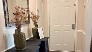 A hallway with a dark wooden desk, two vases with dried flowers, a mirror, and a white door. - Relax and Unwind near West Point Lake (LaGrange)