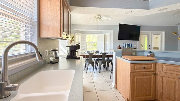A modern kitchen with a large sink, wooden cabinets, a dining area with chairs, and a ceiling fan. - Wonderful 4-bedroom building with AC in charming Port Charlotte (Port Charlotte)