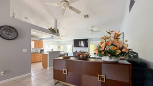 Uma cozinha moderna com uma ilha central, uma área de jantar com mesa de madeira e um espaço de estar com um vaso decorativo.