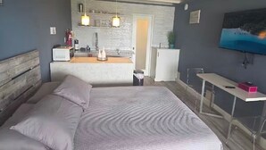 Une chambre moderne avec un grand lit, un petit bureau, une télévision et un coin cuisine.