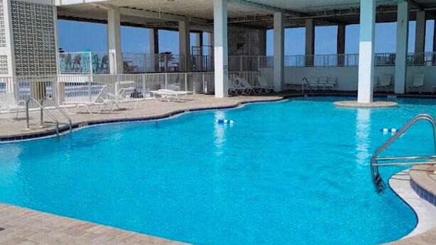 Une piscine intérieure à l’eau d’un bleu cristallin, entourée de chaises longues et d’un espace abrité doté de grandes fenêtres.