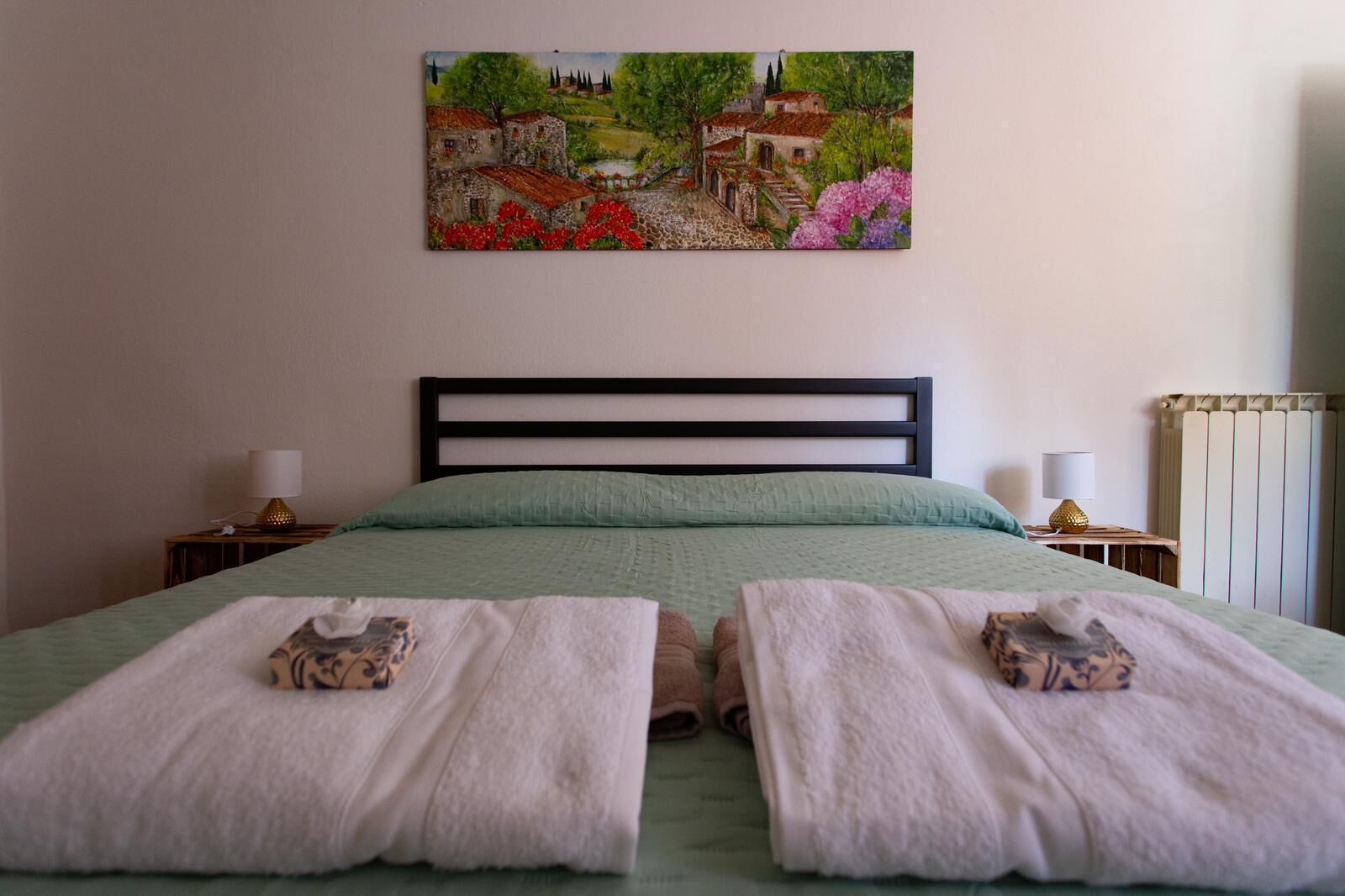 A bedroom with a bed, two bedside tables, a painting on the wall, and a radiator.