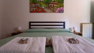 A bedroom with a bed, two bedside tables, a painting on the wall, and a radiator.