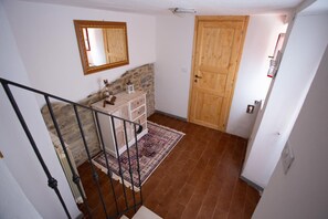 A staircase leading to a room with a stone wall, a wooden door, and a white dresser with a patterned rug.