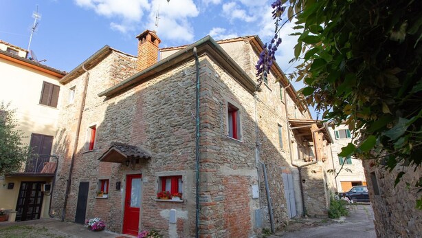 A stone building with a red door, windows with shutters, and a small garden area with flowers. - Apartment not far from the center of Arezzo, suitable for both couples and families (Arezzo)