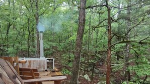 Eine rustikale Holzdiele mit Whirlpool und einem Schornstein, aus dem Dampf aufsteigt, umgeben von dichtem Wald.