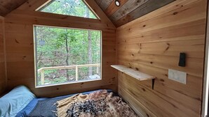 Eine Hütte mit großem Fenster, einem Bett, einem Regal und einer Deckenleuchte.