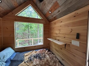 A cabin with a large window, a bed, a shelf, and a ceiling light. - Tiny home with AC in Jasper and Wood Burning Hot Tub (Jasper)