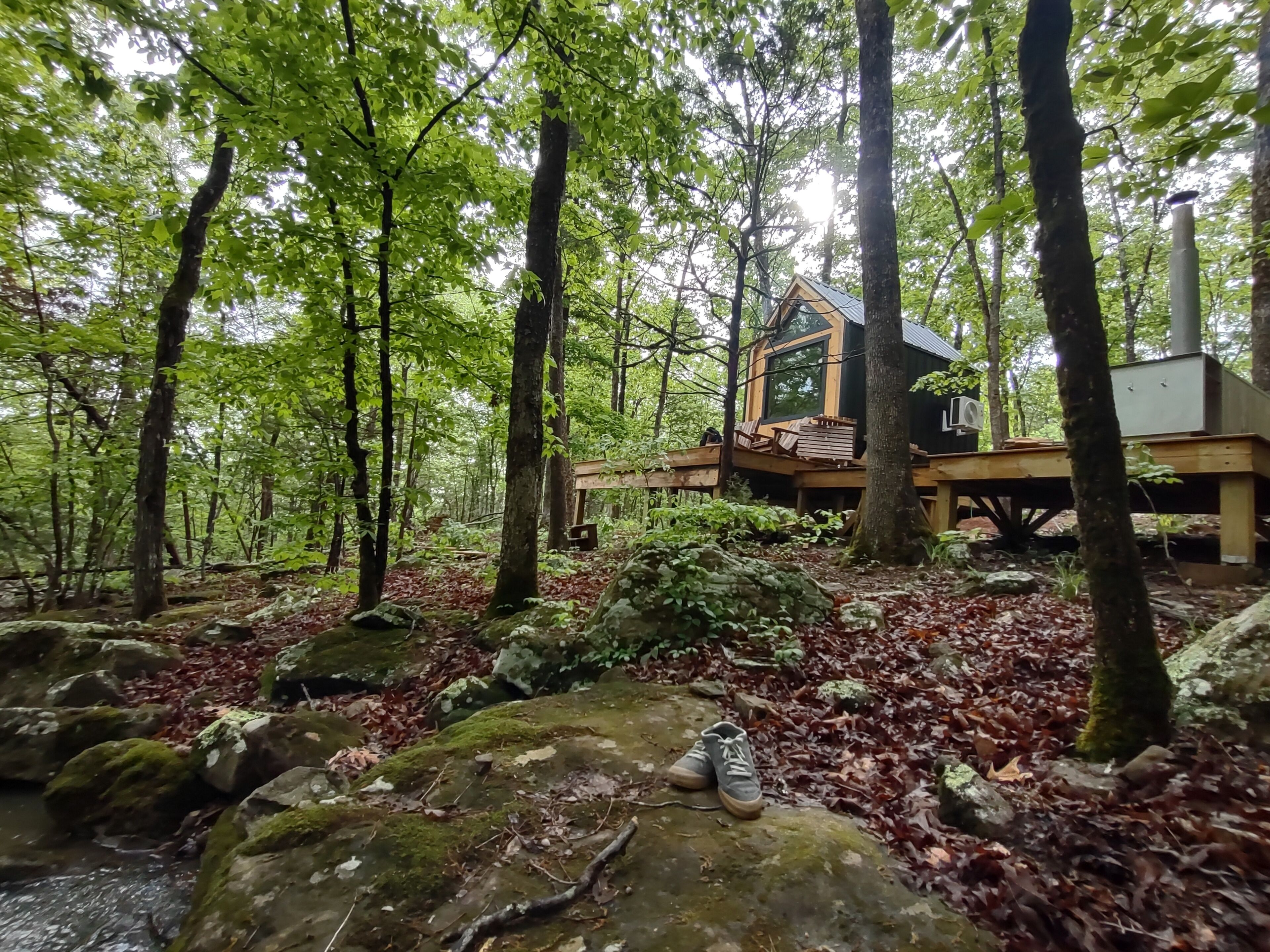 A cabin in a forest with a deck and a chimney.