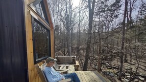 Eine Person sitzt auf einer Holzterrasse mit Blick auf ein bewaldetes Gebiet.