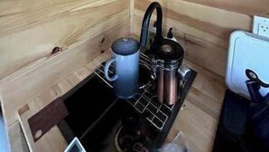 Eine kompakte Küche mit Herd, Wasserkocher und einer Ablage mit Behältern.