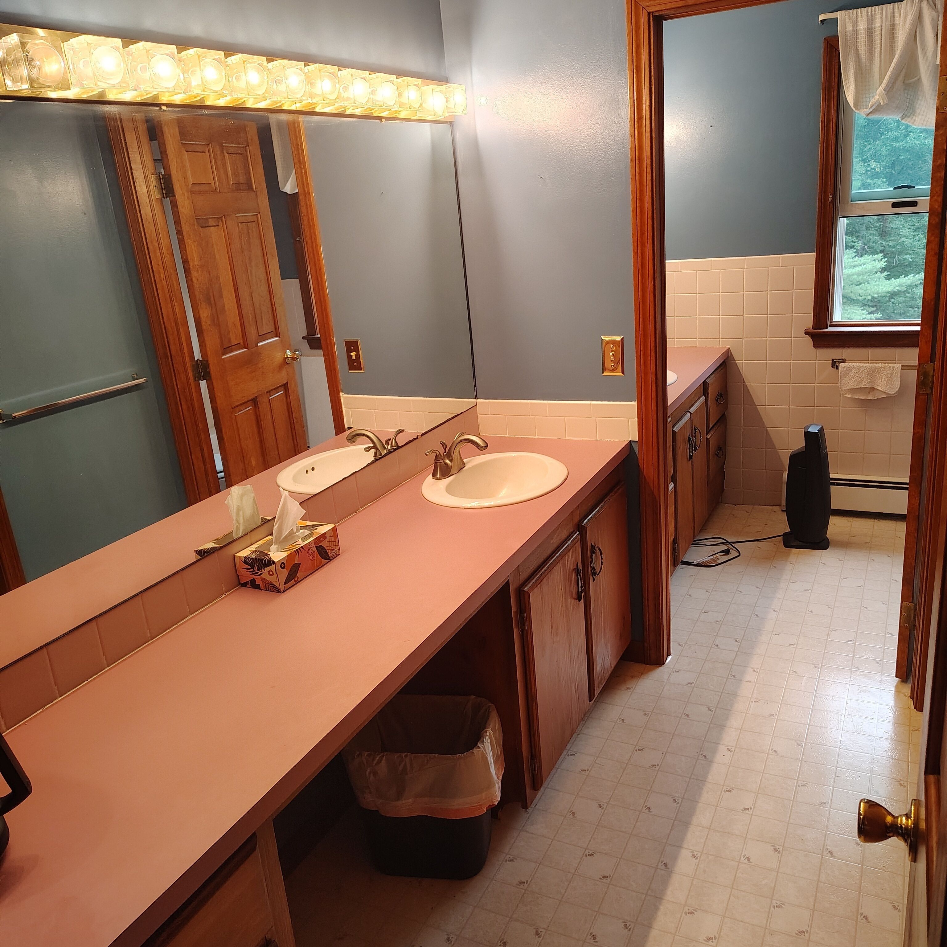 A bathroom with a long vanity, two sinks, a mirror, and a window.