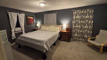 Un dormitorio con una cama, lámparas de noche, una silla y un ventanal con cortinas.