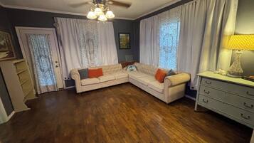 A living room with a sectional sofa, a ceiling fan, a lamp, and a dresser.