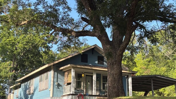 Une maison à deux étages avec un porche, un grand arbre et une zone de porche couverte.