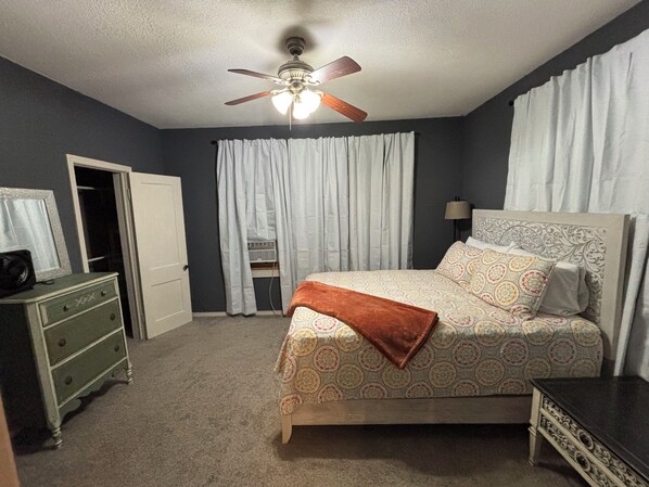 A bedroom with a bed, a dresser, a ceiling fan, and a window with curtains.