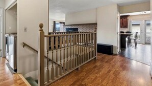 Un vaste espace de vie doté d’un plancher en bois, d’un escalier avec une rampe et d’une cuisine à l’arrière-plan.
