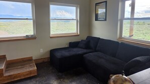 A room with a large window, a wooden bench, and a dark-colored sofa. - Wonderful 3-bedroom house in Dubois perfect for your getaway peace and quiet (Dubois)