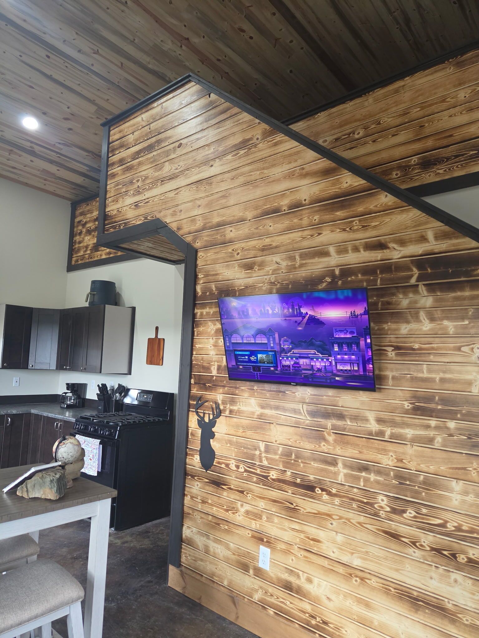 A kitchen with wooden paneling, a TV mounted on the wall, and a dining area with a table and chairs.