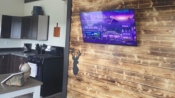 A kitchen with wooden paneling, a TV mounted on the wall, and a dining area with a table and chairs. - Wonderful 3-bedroom house in Dubois perfect for your getaway peace and quiet (Dubois)