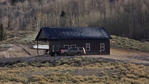 A small cabin with a metal roof, a covered area with a table and chairs, and a vehicle parked in front. - Wonderful 3-bedroom house in Dubois perfect for your getaway peace and quiet (Dubois)