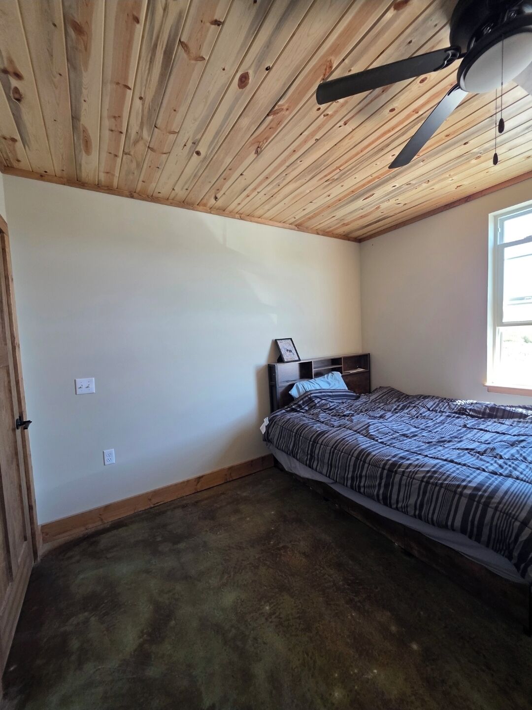 Une chambre à coucher avec un plafond en bois, un lit recouvert d’une couvre-lit à rayures, une table de chevet et une fenêtre.