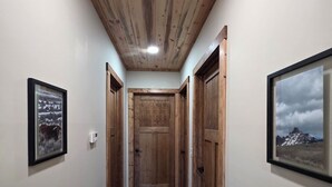 A narrow hallway with wooden walls and ceiling, a door at the end, and framed pictures on the walls. - Wonderful 3-bedroom house in Dubois perfect for your getaway peace and quiet (Dubois)