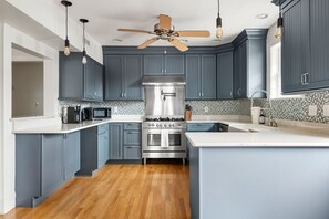 A kitchen with blue cabinets, a stainless steel stove, and a ceiling fan. - Blackbeard's Isle -  9 beds, 6BR/3BA - 500 ft from Beach (Isle of Palms)