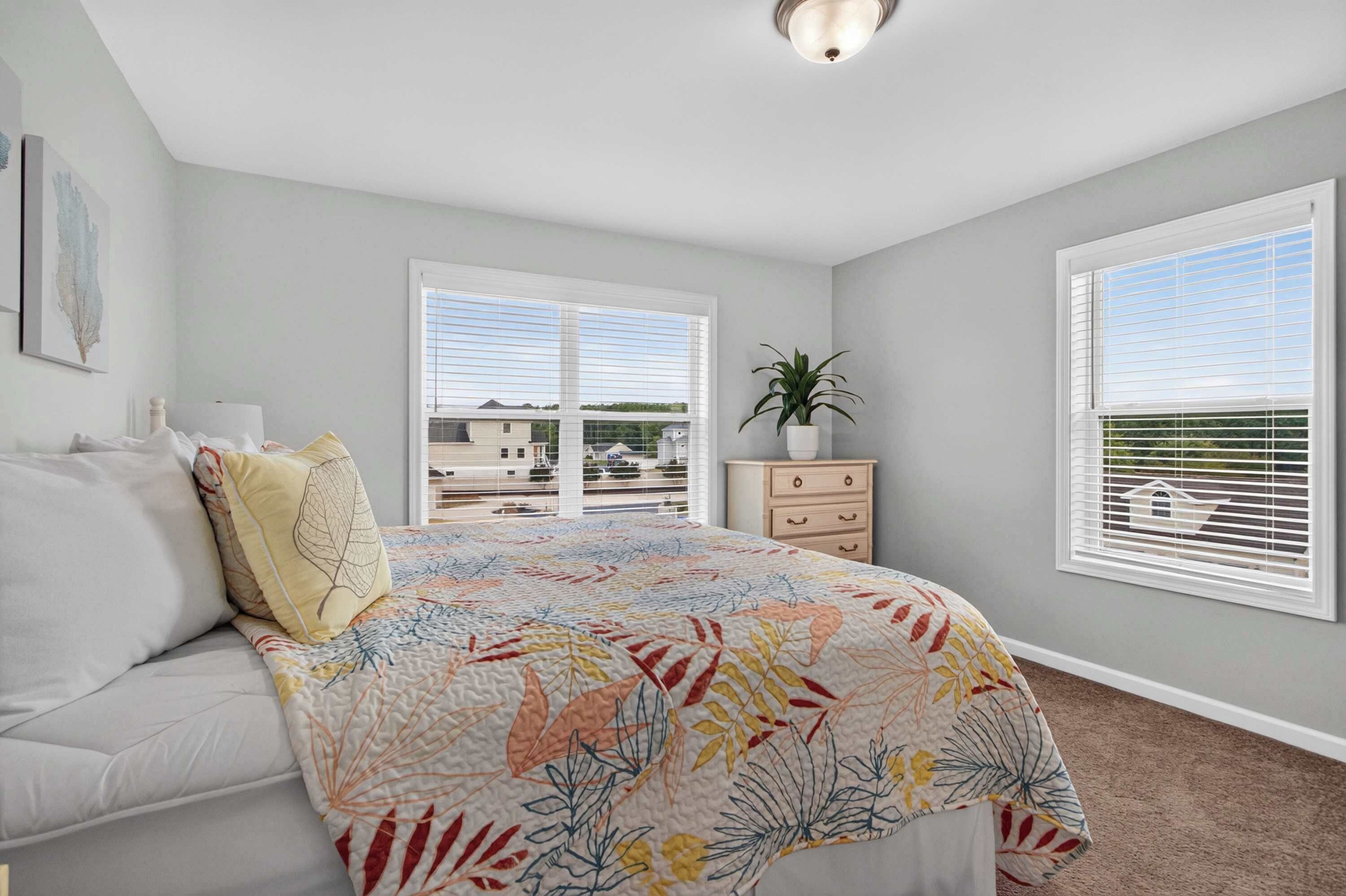 A bedroom with a bed, a dresser, a potted plant, and a window with blinds.