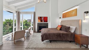 A bedroom with a large bed, a fireplace, a TV, and a view of greenery through the window. - Newly updated 3-bedroom/3-bath beachfront house on the peninsula in Long Beach (Long Beach)