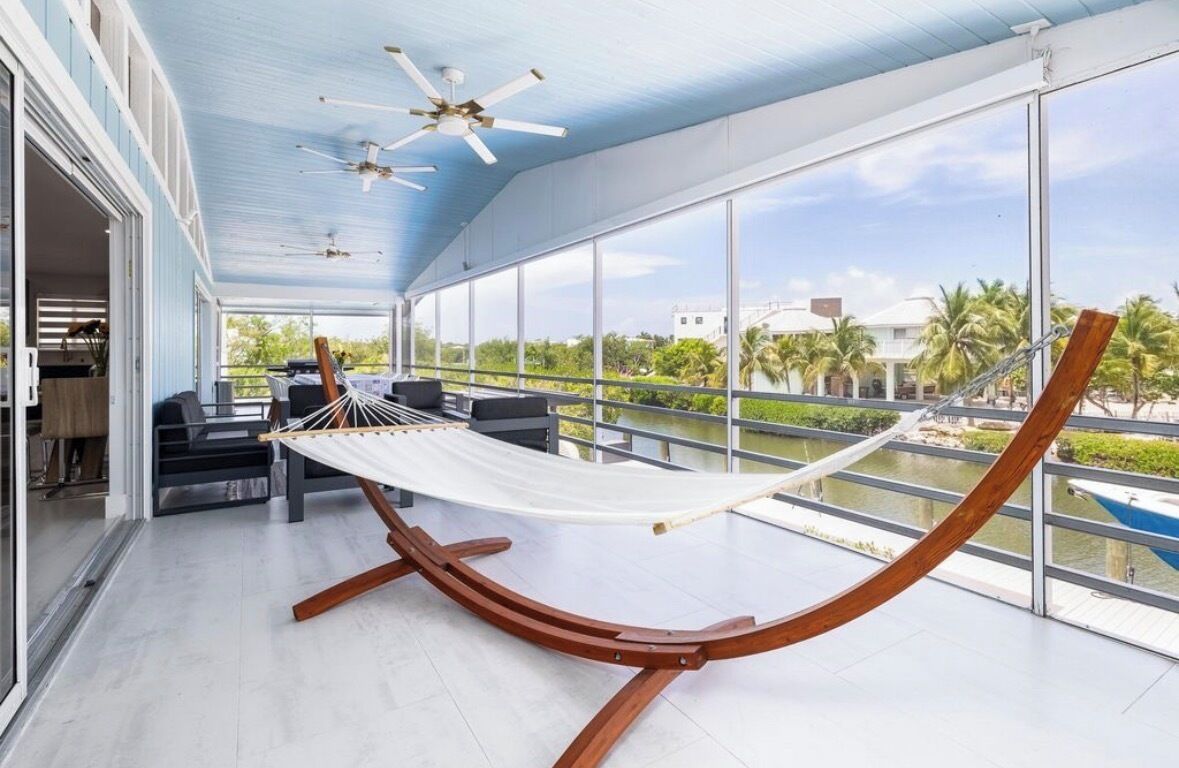 A hammock in a spacious room with large windows, a ceiling fan, and a view of a water body.