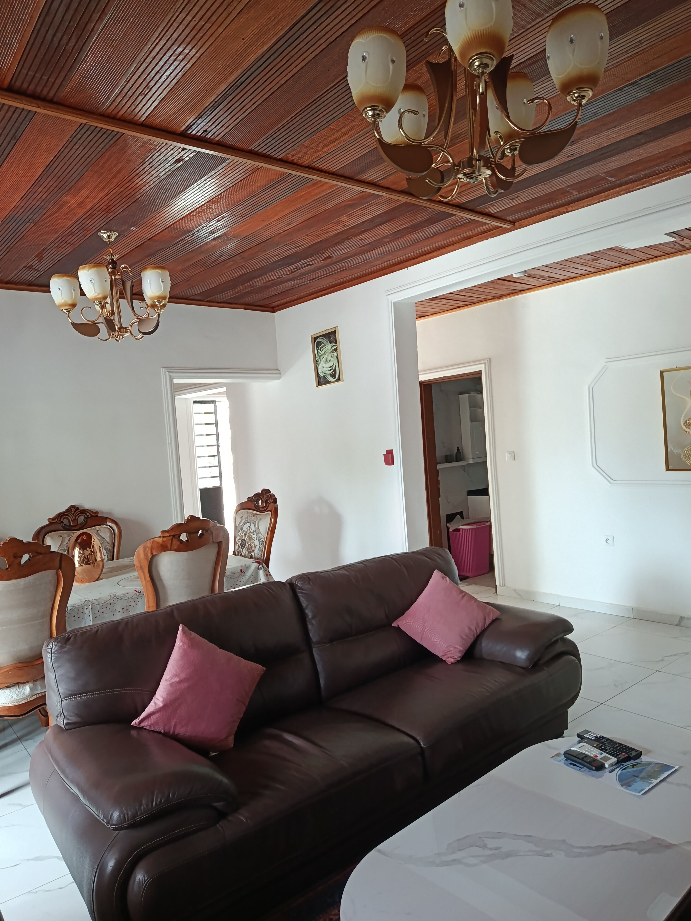 Una sala de estar con un sofá de cuero marrón, una araña y un comedor con sillas de madera.