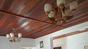 A living room with a brown leather sofa, a chandelier, and a dining area with wooden chairs.