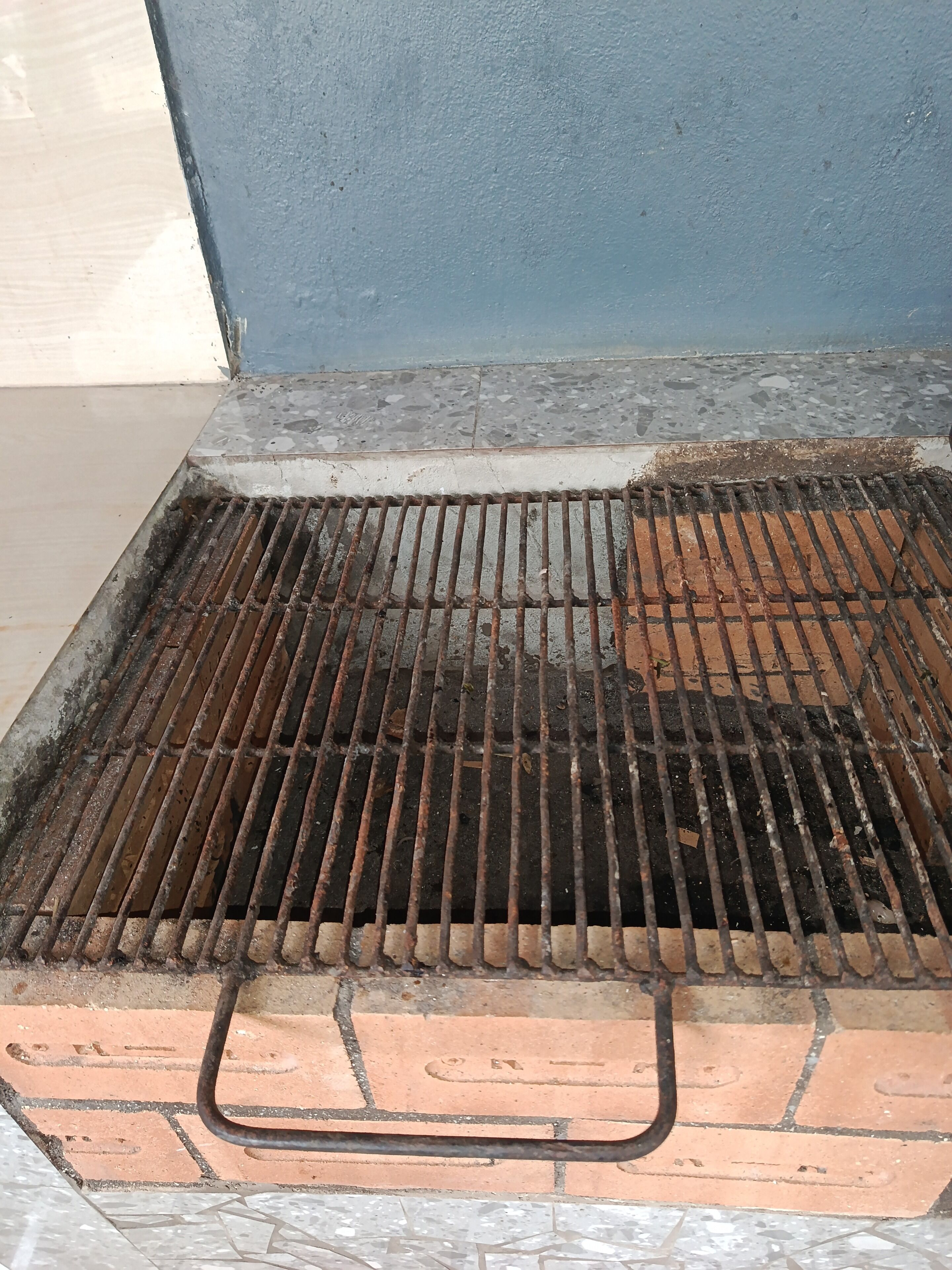 A grill with a metal grate, a handle, and a brick base.