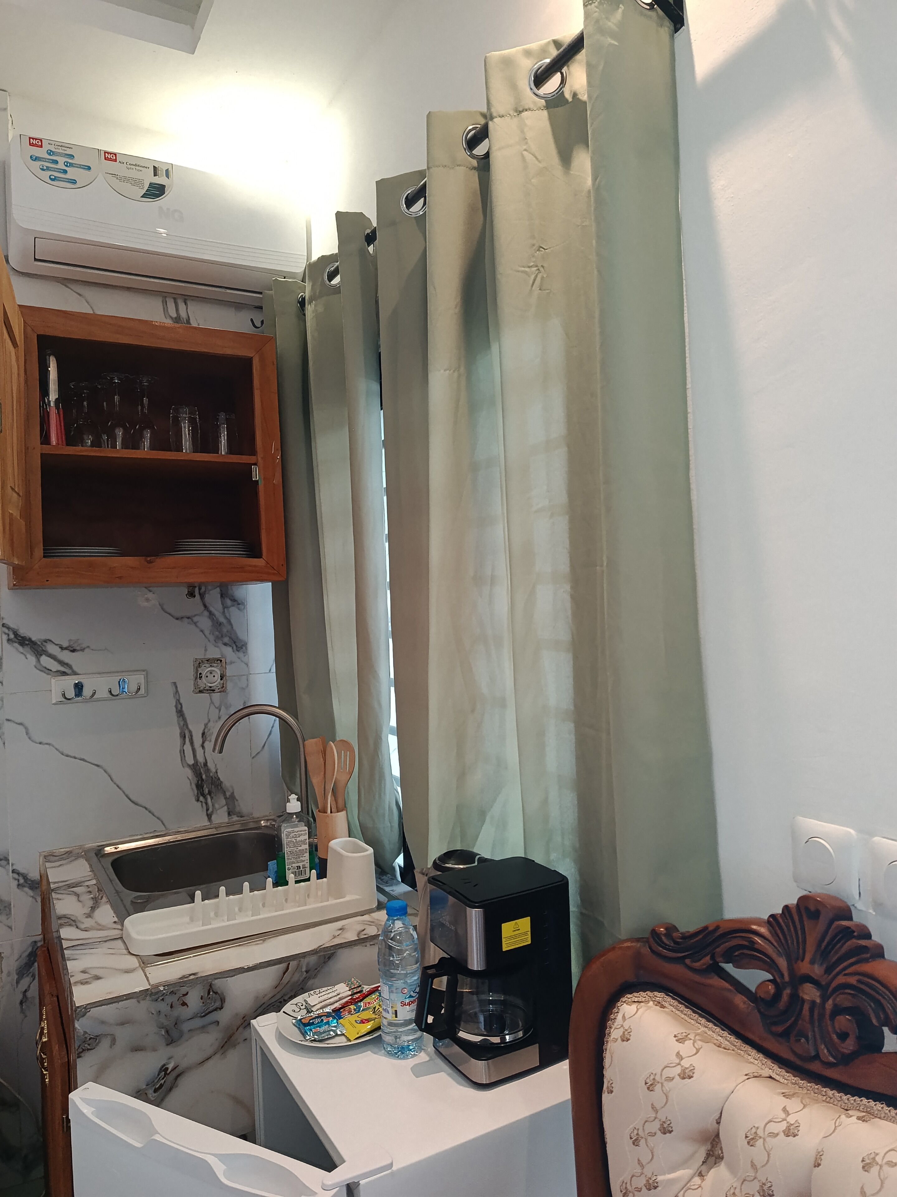 A kitchen with a marble backsplash, a coffee maker, a water bottle, and a cabinet with glassware.