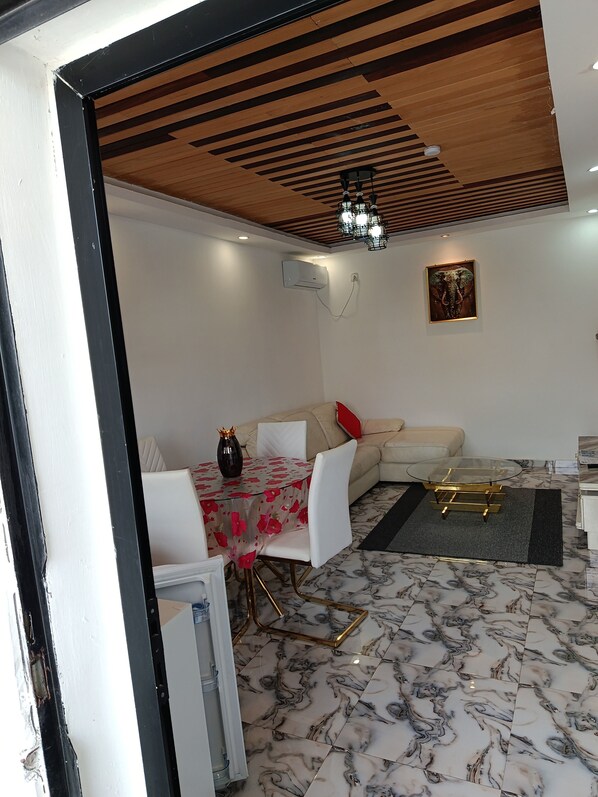 A living room with a dining table, sofa, marble flooring, and a ceiling fan.