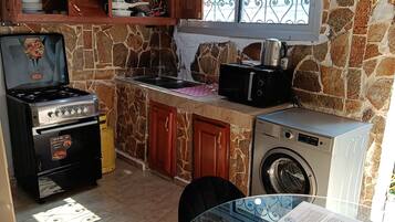 Une cuisine avec un mur en pierre, une cuisinière à gaz, un four à micro-ondes, un lave-linge et une table en verre avec un magazine.