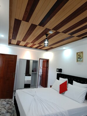 A bedroom with a wooden ceiling, a bed with white bedding and a red pillow, a wardrobe, and a bathroom visible through an open door.