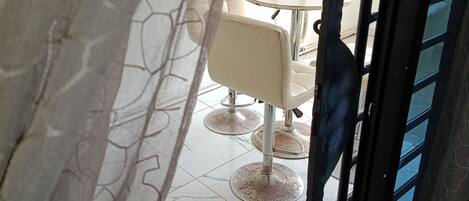 A view through a doorway with a patterned curtain, leading to a room with a white table and two chairs.