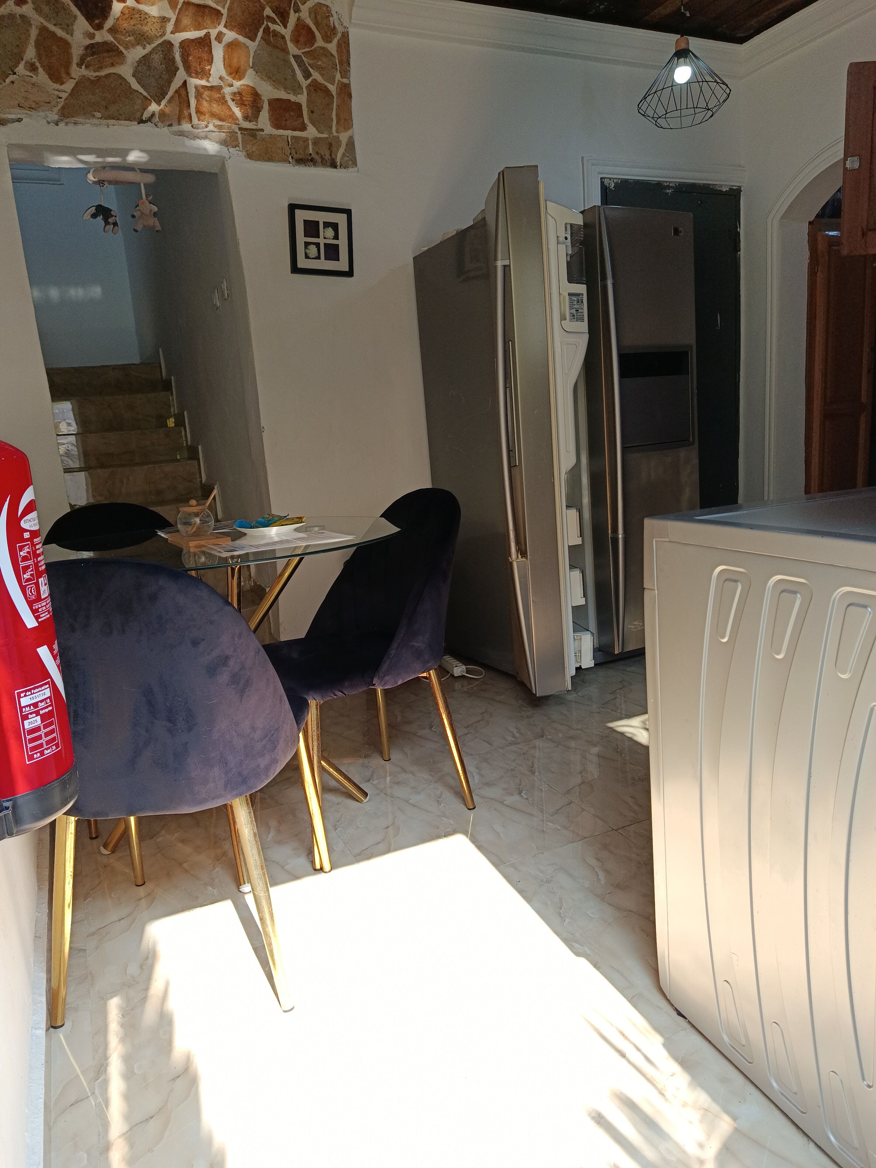 A kitchen with a refrigerator, a dining table with chairs, and a stone wall.