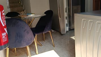 A kitchen with a refrigerator, a dining table with chairs, and a stone wall.