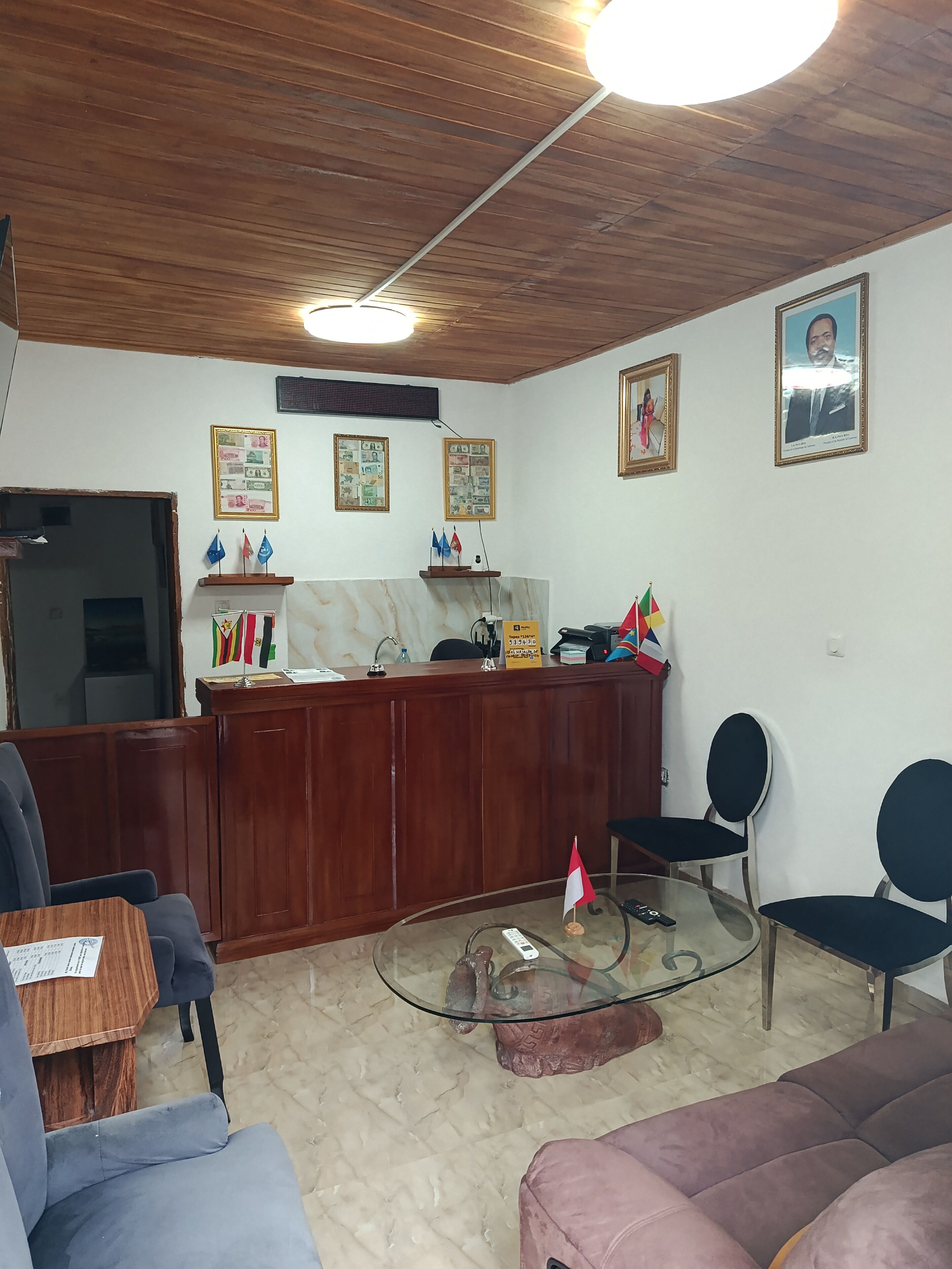 Un espace d’accueil comprenant un bureau en bois, des chaises, une table basse en verre et un ventilateur de plafond.