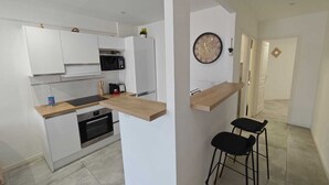 Eine moderne Küche mit weißen Schränken, einer Mikrowelle und einem eingebauten Backofen. Es gibt eine Holzarbeitsplatte und einen schwarzen Stuhl.
